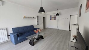 Un soggiorno moderno con un divano blu, un tavolino in vetro e una lampada a sospensione nera.