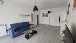 A modern living room with a blue sofa, a glass coffee table, and a black pendant light.