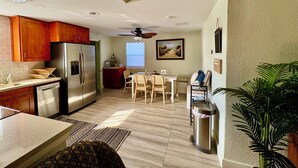 A compact kitchen with wooden cabinets, a stainless steel refrigerator, and a dining area with a table and chairs. - Private Delray Beach Pool Home Near Atlantic Avenue, Dining & Beach (Delray Beach)