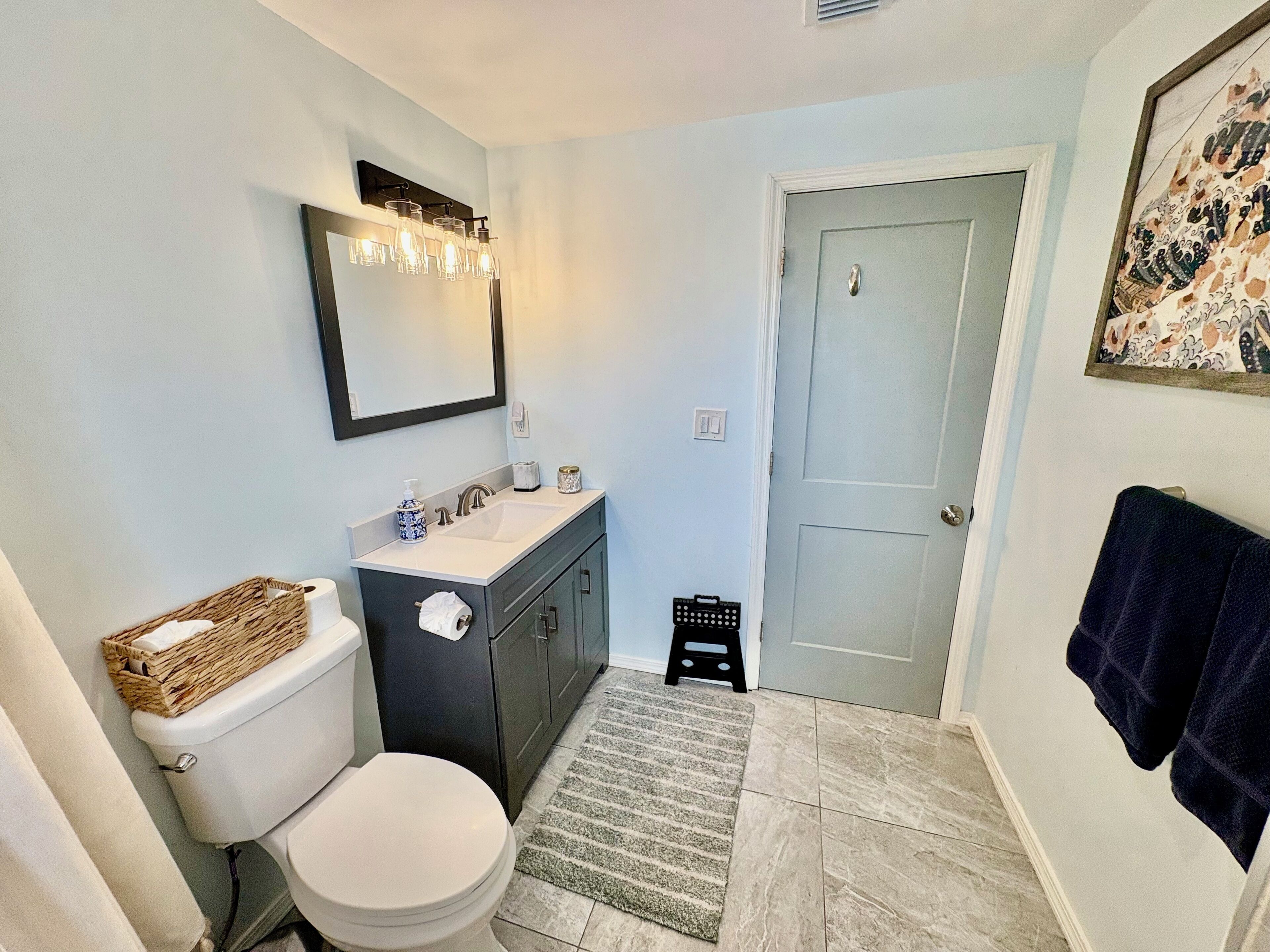 A bathroom with a toilet, sink, and mirror. There is a door and a towel rack.