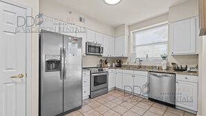 A modern kitchen with stainless steel appliances, white cabinets, and a tiled floor.