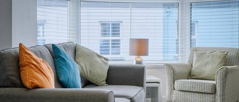 A modern living room with a grey sofa, a patterned armchair, and a lamp.