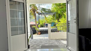 Amplia habitación con un gran ventanal corredera que da a un espacio exterior con patio empedrado, zona de estar cubierta y abundante vegetación.