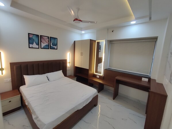 A modern bedroom with a large bed, bedside tables, a desk, a wardrobe, and a ceiling fan. - Vinci Suites (Nagpur)