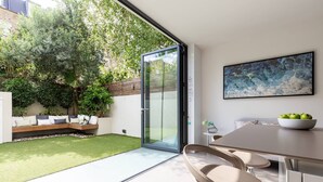 Une terrasse moderne avec une porte vitrée donnant sur un jardin, un coin repas avec une table et des chaises, et un tableau accroché au mur.