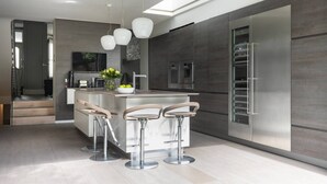 Une cuisine moderne dotée d’un îlot central, de tabourets de bar, d’appareils électroménagers en acier inoxydable et d’une verrière.