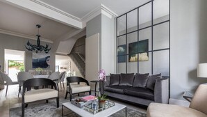 Un salon moderne avec un canapé gris, des chaises noires et blanches, une table basse en verre et un escalier menant à une autre pièce.
