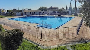 A rectangular swimming pool with a tiled deck and metal railing, surrounded by a fence.