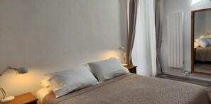 A bedroom with a bed, two bedside lamps, a mirror, and a radiator. - Entire Historic Villa,  Casa Nobre with Patio and Roof Top in the Historic Area (São Brás de Alportel)