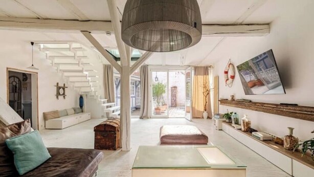 A spacious living area with a modern sofa, a glass coffee table, and a hanging light fixture. A staircase with white railings leads to an outdoor area. - Stilhaus 1730 - Central. Quiet. Unique. 1st floor (Königsbach-Stein)