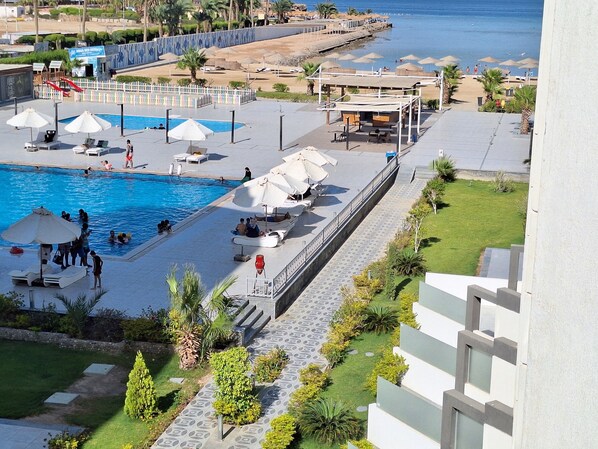 A pool area with lounge chairs and umbrellas, a small boat, and a view of the beach and ocean.