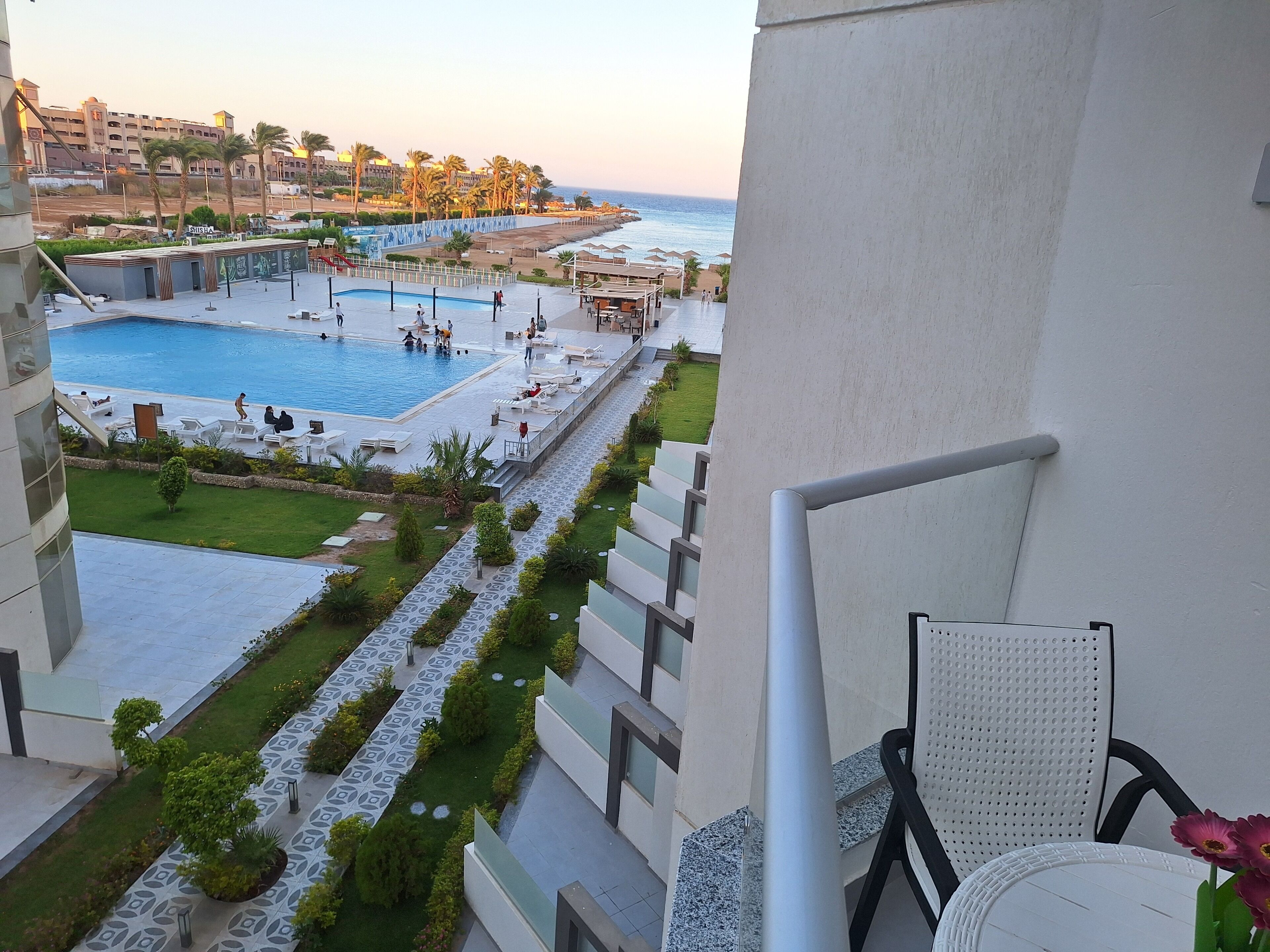 A pool area with a view of the sea, a grassy pathway, and a seating area with chairs.