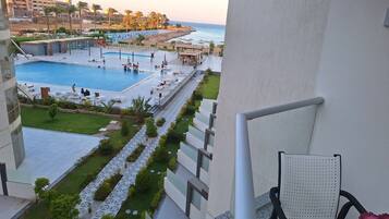 A pool area with a view of the sea, a grassy pathway, and a seating area with chairs.