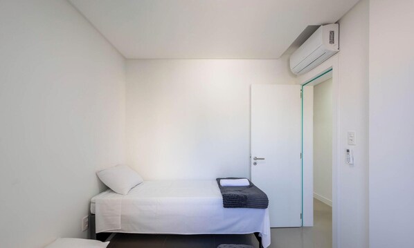 Una habitación pequeña y limpia con cama, mesita de noche y puerta.