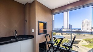Un balcon avec un coin cuisine, une fenêtre donnant sur le paysage urbain et une table avec des chaises.