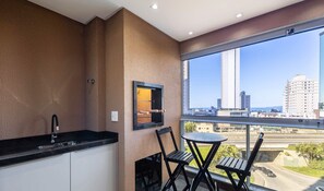 Un balcon avec un coin cuisine, une fenêtre donnant sur le paysage urbain et une table avec des chaises.