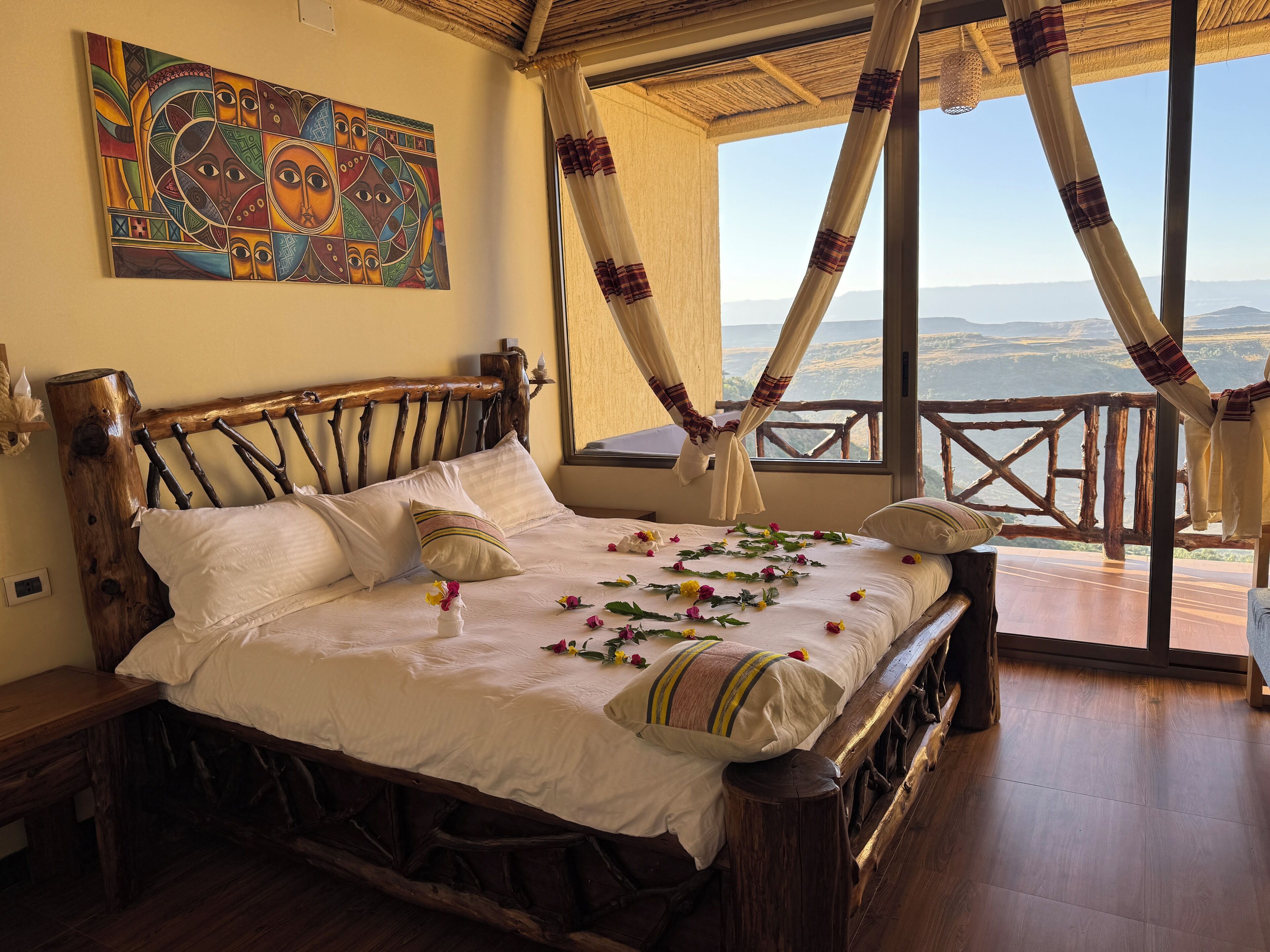 A bed with a canopy, a painting on the wall, and a view of the landscape through large windows.