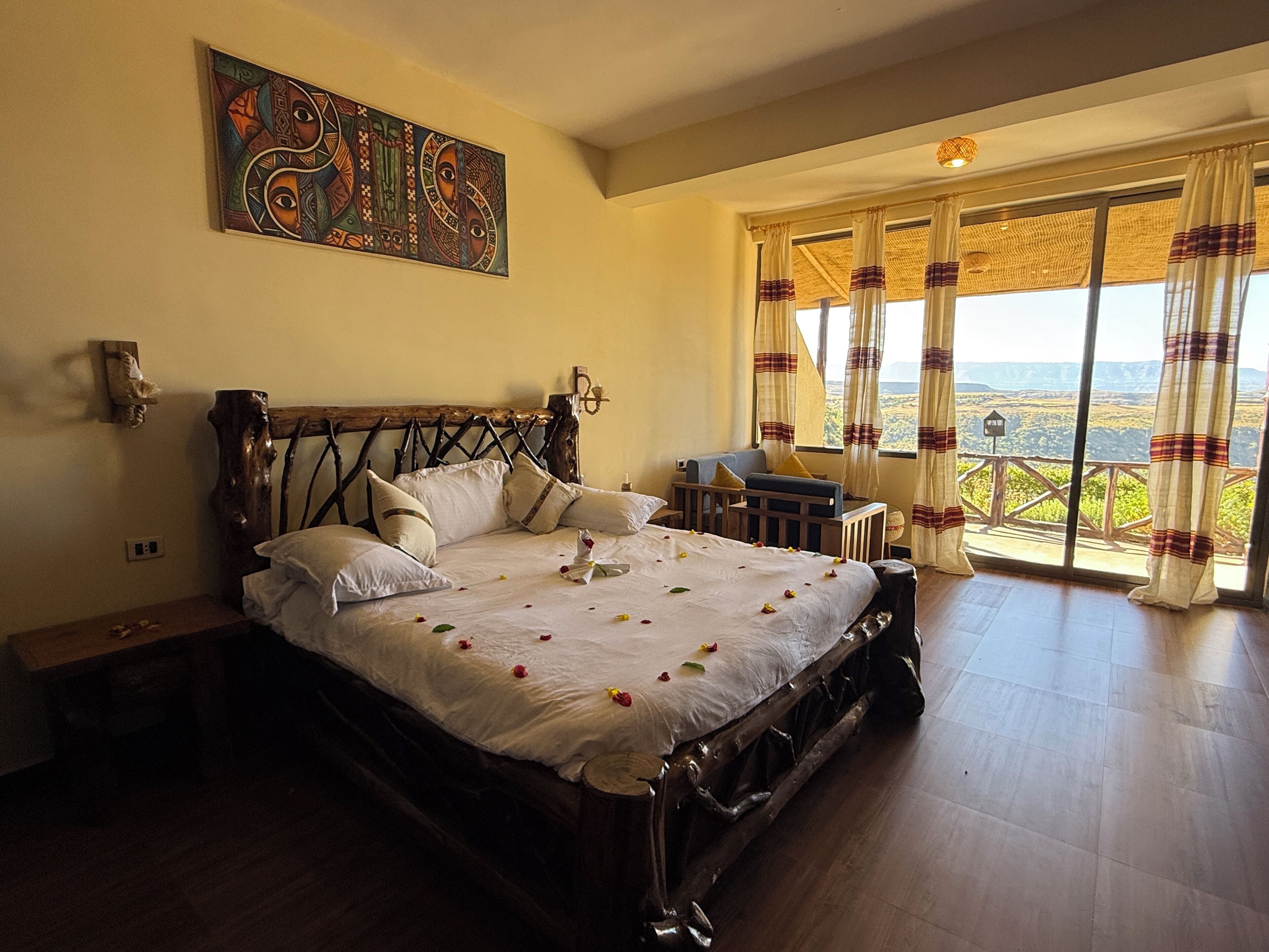 A spacious bedroom with a large bed, a wooden headboard, and a view of the landscape through large windows.