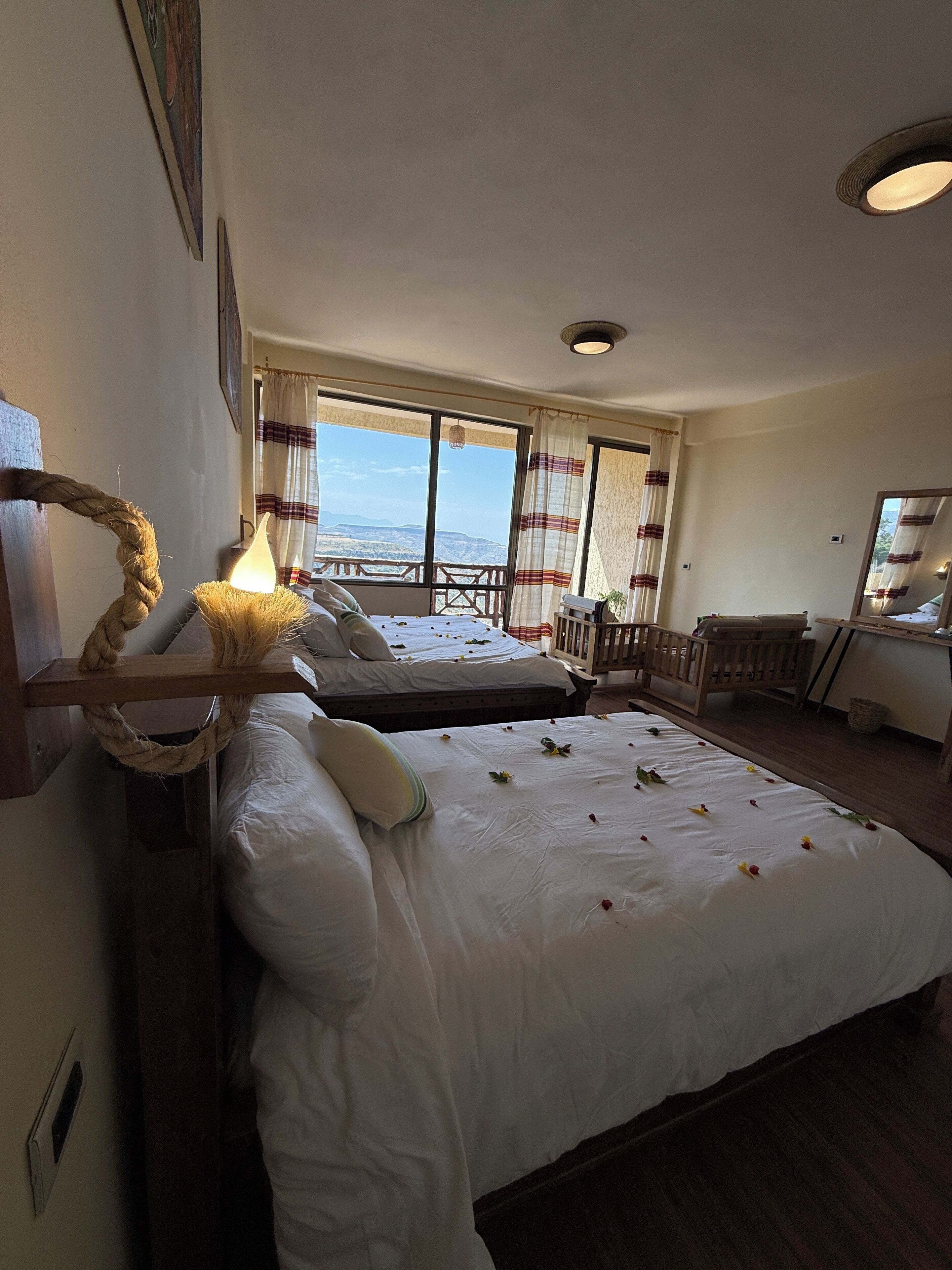 A bedroom with two beds, a view of the mountains, a wooden headboard, and a bedside lamp.