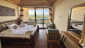 A bedroom with a bed, a small table, a chair, and a balcony with a view. - Hilltop Lodge - Lalibela  (Lalibela)