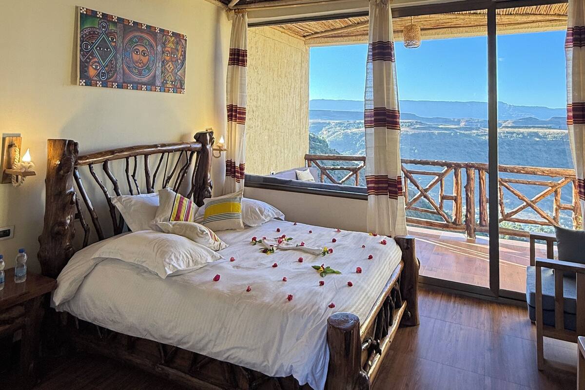 Una habitación rústica de madera con una cama, una mesita de noche, un cuadro y un balcón con vistas.