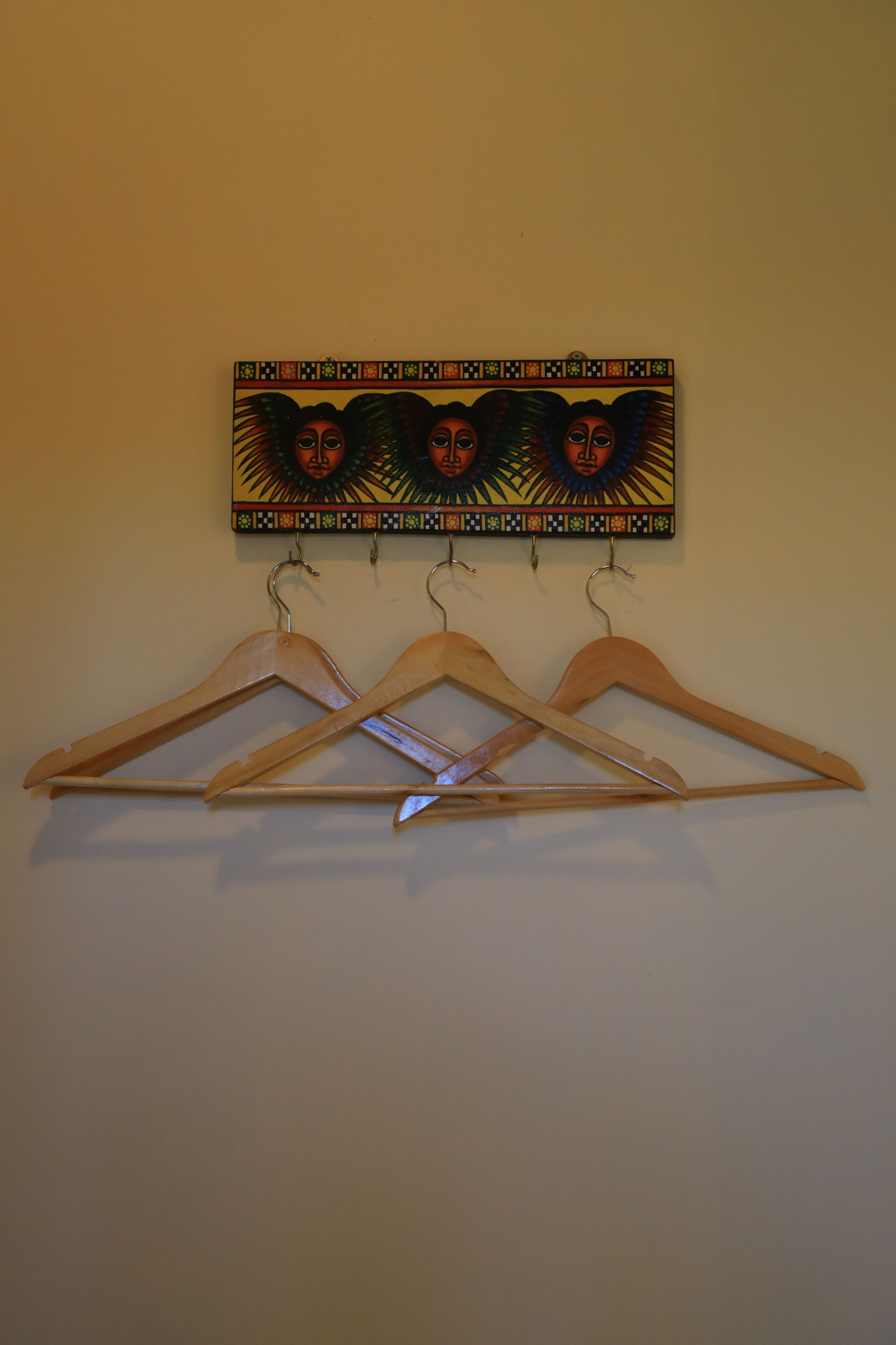 Un perchero de madera fijado a la pared con tres colgadores y un adorno decorativo encima.