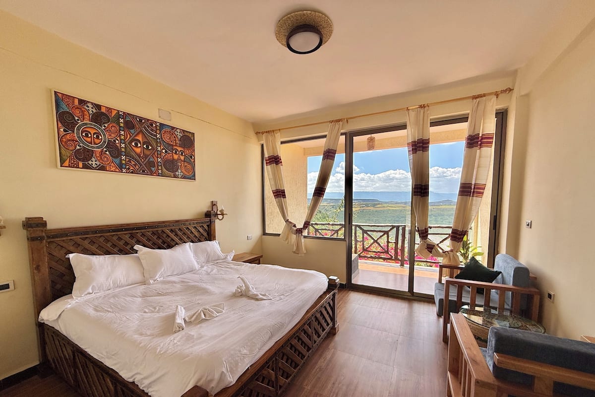 Un dormitorio con una cama de madera, un cuadro grande en la pared y un balcón con cortinas.