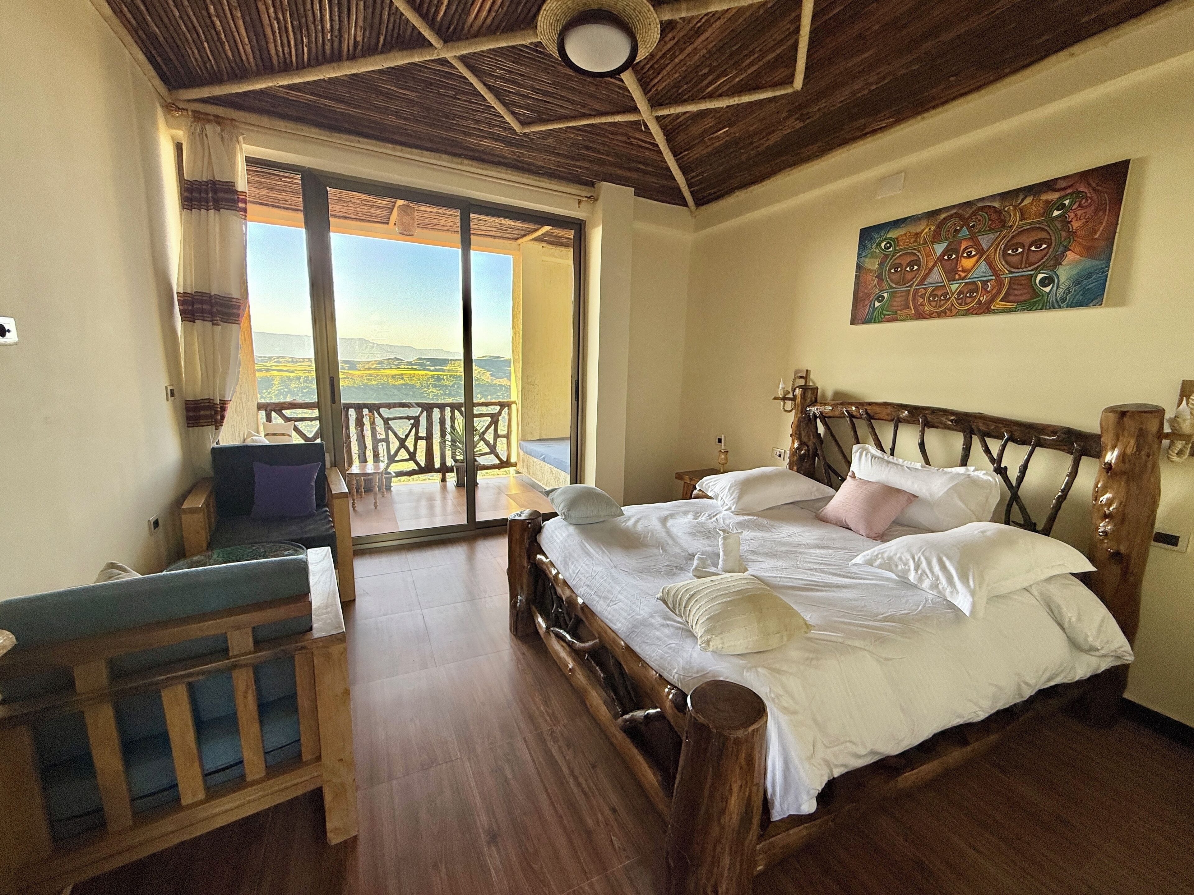 Een slaapkamer met een houten bed, een balkon met uitzicht op het landschap en een schilderij aan de muur.
