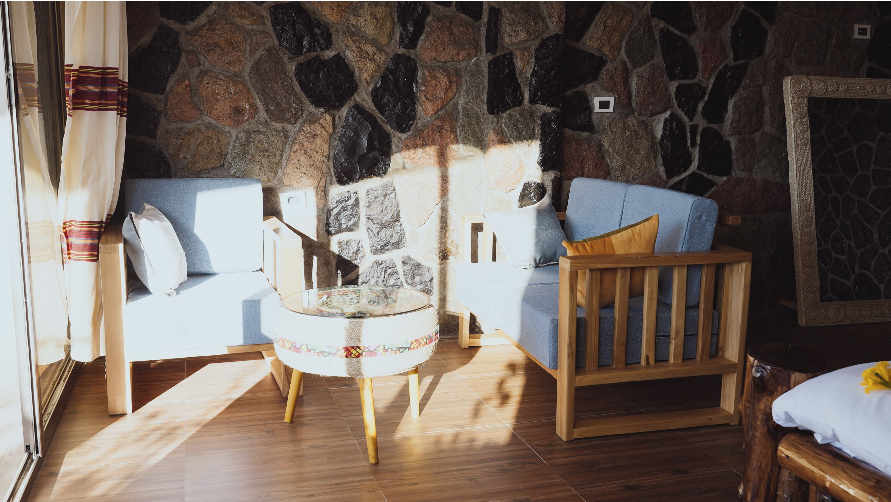 A cozy room with a stone wall, a wooden floor, a round table, and a blue sofa with a wooden chair.