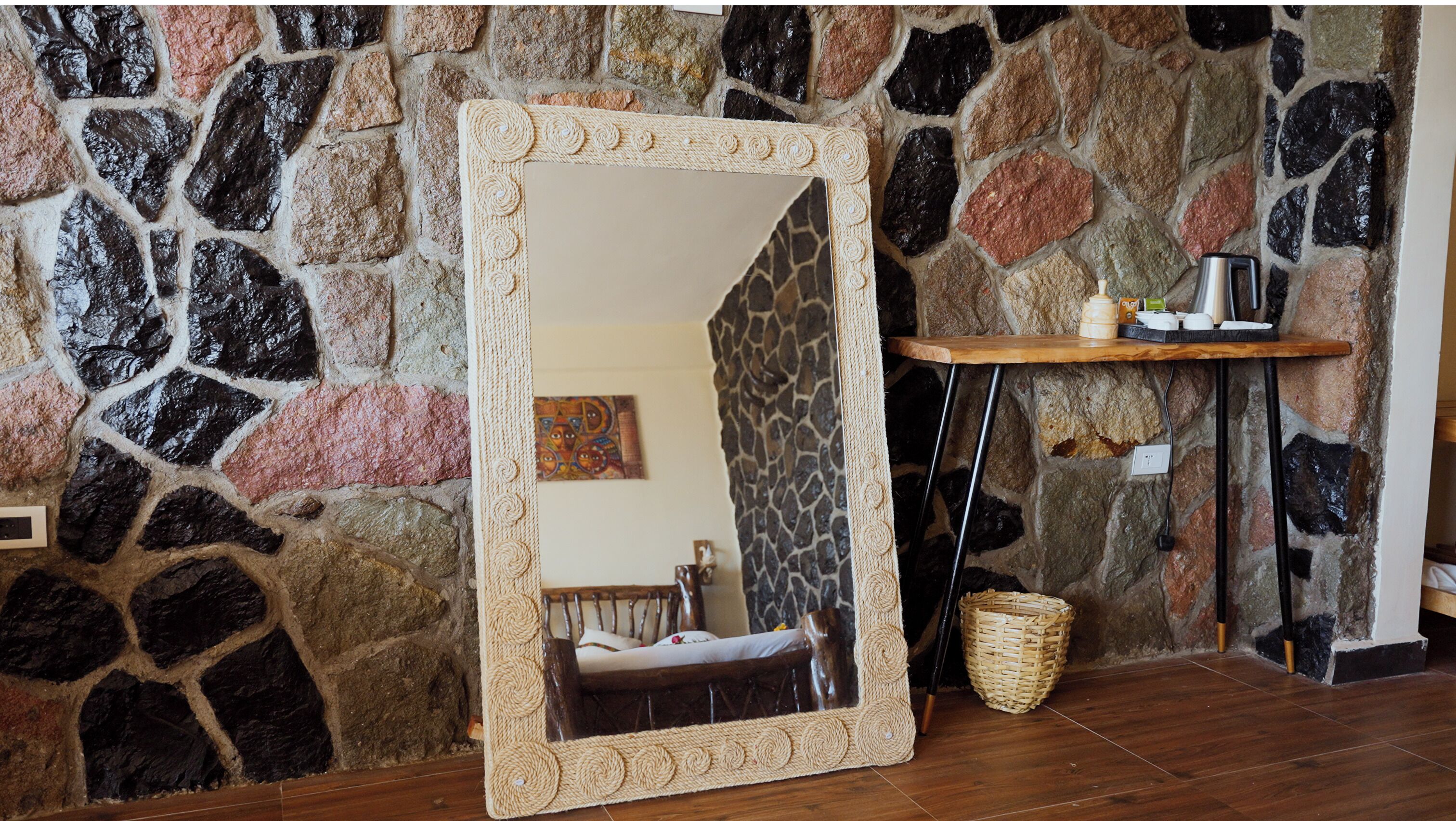 A room with a stone wall, a large mirror, a wooden bench, and a small table with a kettle and cups.