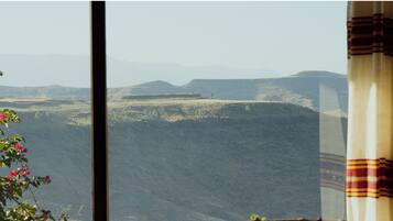 A view of a mountainous landscape through a window with a curtain partially visible on the right.