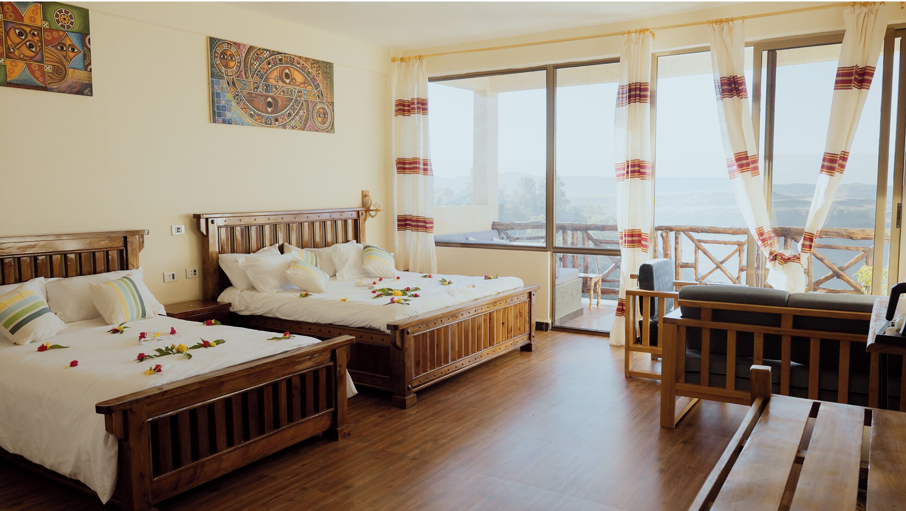 Een kamer met twee houten bedden, een balkon met houten leuning en een groot raam met gordijnen.