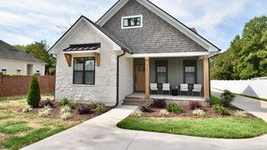 A modern two-story house with a stone facade, a grey shingled roof, and a front porch with two chairs.