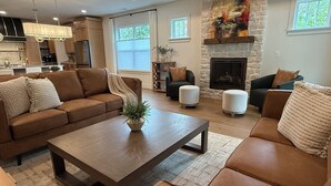 A spacious living room with a brown leather sofa, a wooden coffee table, and a stone fireplace.