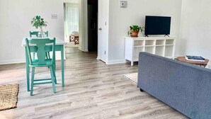 A living room with a grey sofa, a teal chair, a TV on a white stand, and a potted plant. - Classy vacay stay at Swansboro (Swansboro)