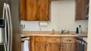 A kitchen with wooden cabinets, a stainless steel refrigerator, and a wooden floor. - Classy vacay stay at Swansboro (Swansboro)