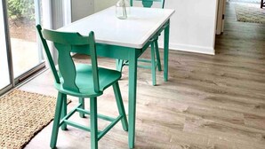 A dining area with a white table and teal chairs, a vase with green foliage, and a view through a large window. - Classy vacay stay at Swansboro (Swansboro)