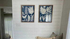A dining area with a round wooden table, black chairs, and two framed botanical prints on the wall. - Cocína Vèrde of #swansboro (Swansboro)