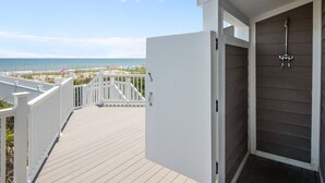 A wooden deck leading to a beach view, a white door, and a small enclosed area with a shower. - Oceanfront home with breathtaking views, West! (Emerald Isle)