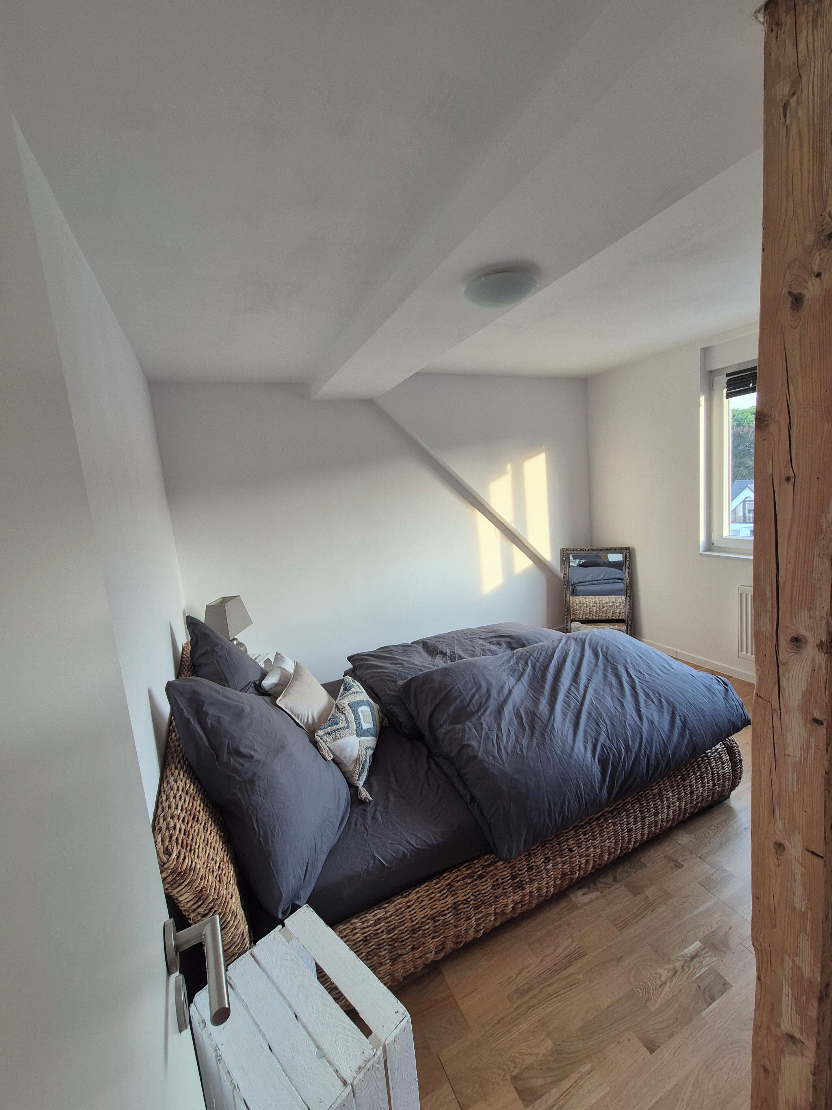 A bedroom with a bed, pillows, a bedside table, a mirror, and a window.