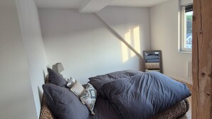 A bedroom with a bed, pillows, a bedside table, a mirror, and a window.