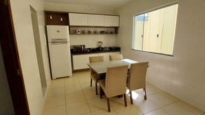 A compact kitchen with a dining table and chairs, a refrigerator, and a window providing natural light. - COPFL0101 - Engenheiro Alves de Souza (Salvador)