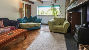A cozy living room with wooden beams, a fireplace, a sofa, a chair, and a window with a view of greenery. - Neuadd Wen (Gaerwen)