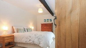 A bedroom with a bed, nightstands, a wooden dresser, and a ceiling light. - Neuadd Wen (Gaerwen)