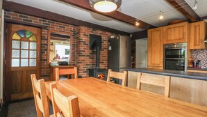 A kitchen with wooden cabinets, a brick wall, a wooden dining table, and a built-in oven. - Neuadd Wen (Gaerwen)