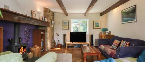 A cozy living room with a fireplace, wooden beams, a television, and comfortable seating.