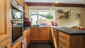 A kitchen with wooden cabinets, a black countertop, and a window providing natural light. - Neuadd Wen (Gaerwen)