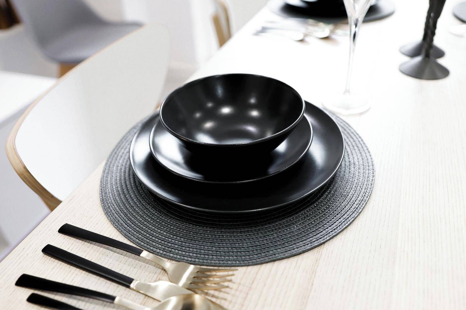 A table set with black plates, a glass, and cutlery.
