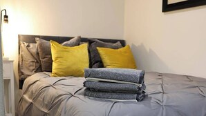Ein ordentlich bezogenes Bett mit einer grauen Bettdecke und mehreren Kissen, darunter eines gelb.