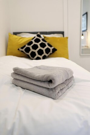 A neatly made bed with a folded gray towel on top, a black and white hexagonal pillow, and a yellow pillow. - 4 Guests - Pet Friendly Retreat in Thornton Heath (Thornton Heath)